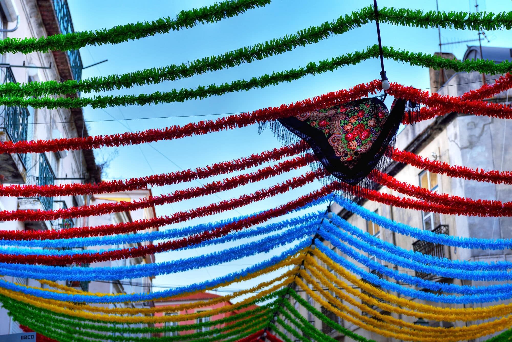 Colourful red, green, blue and yellow festival decorations are strung across a street between buildings.