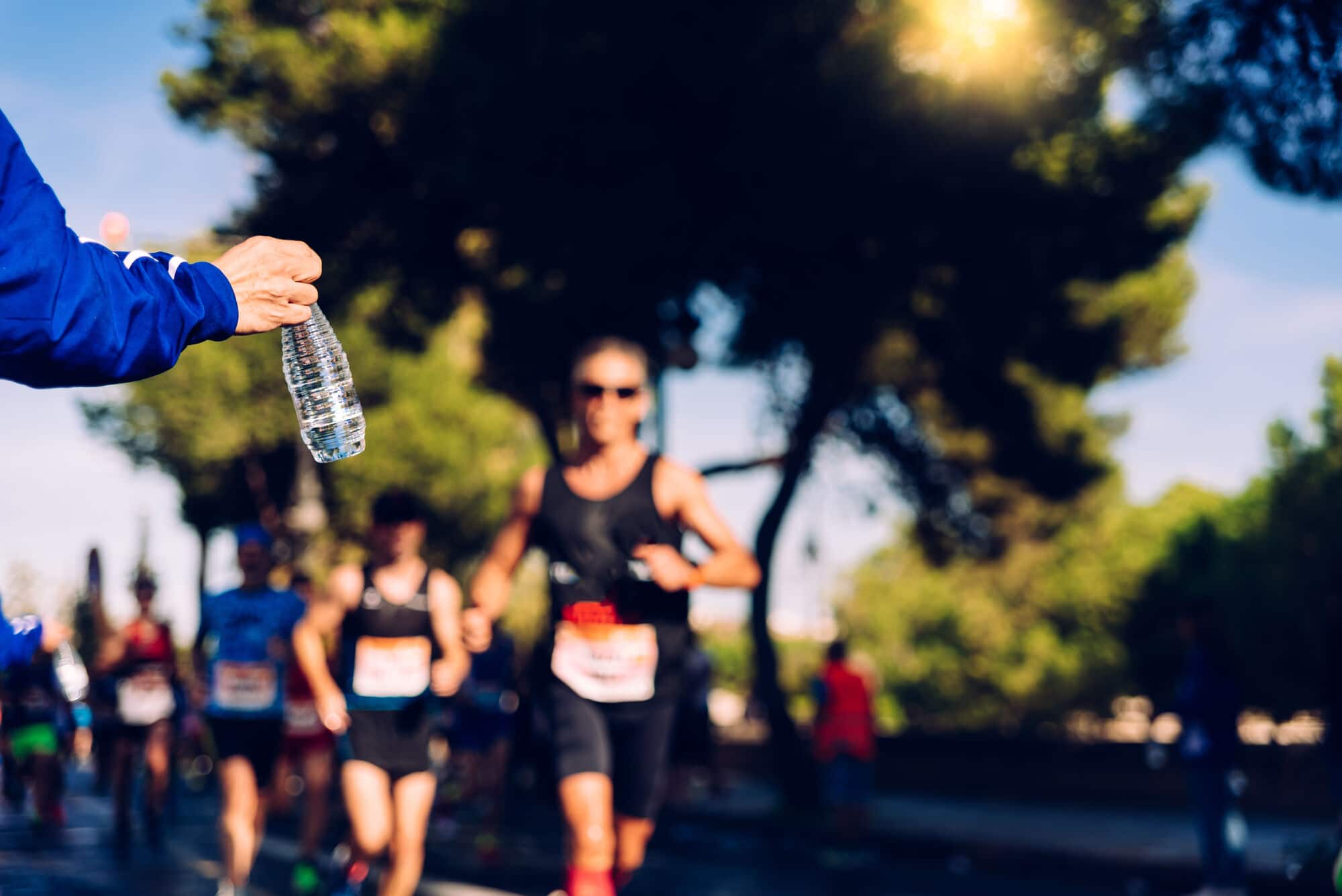Person handing a bottle of water to runners during a marathon in a park.
