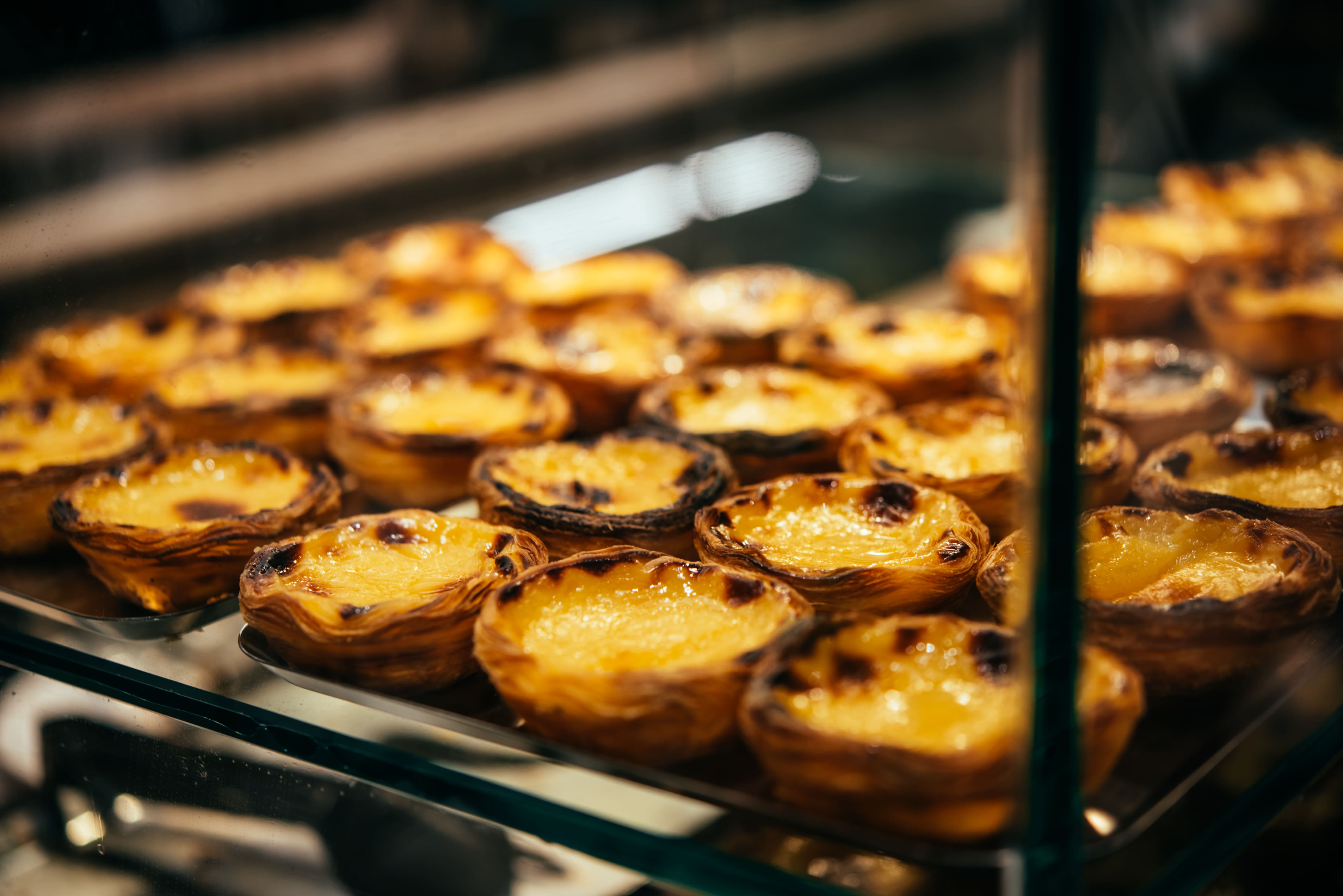 Tray of custard tarts displayed behind glass in a bakery or food counter.