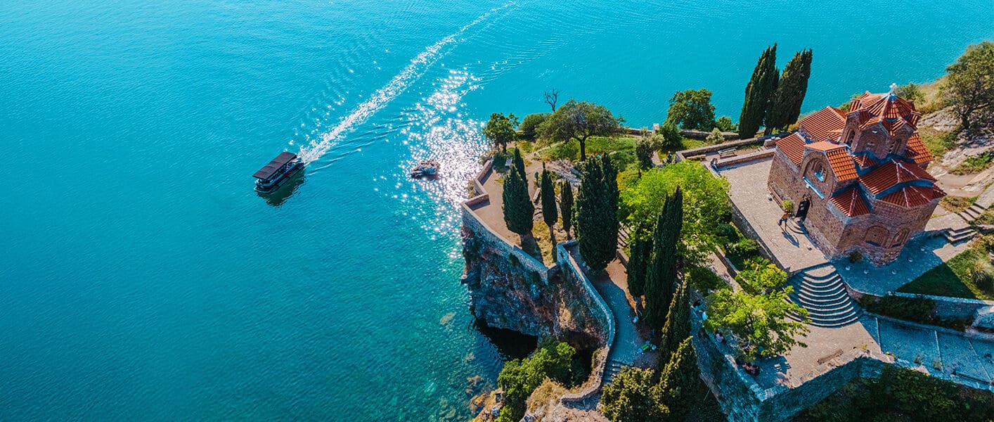 Church of St. John at Kaneo with terracotta roof perched on a cliff overlooking the turquoise waters of Lake Ohrid.