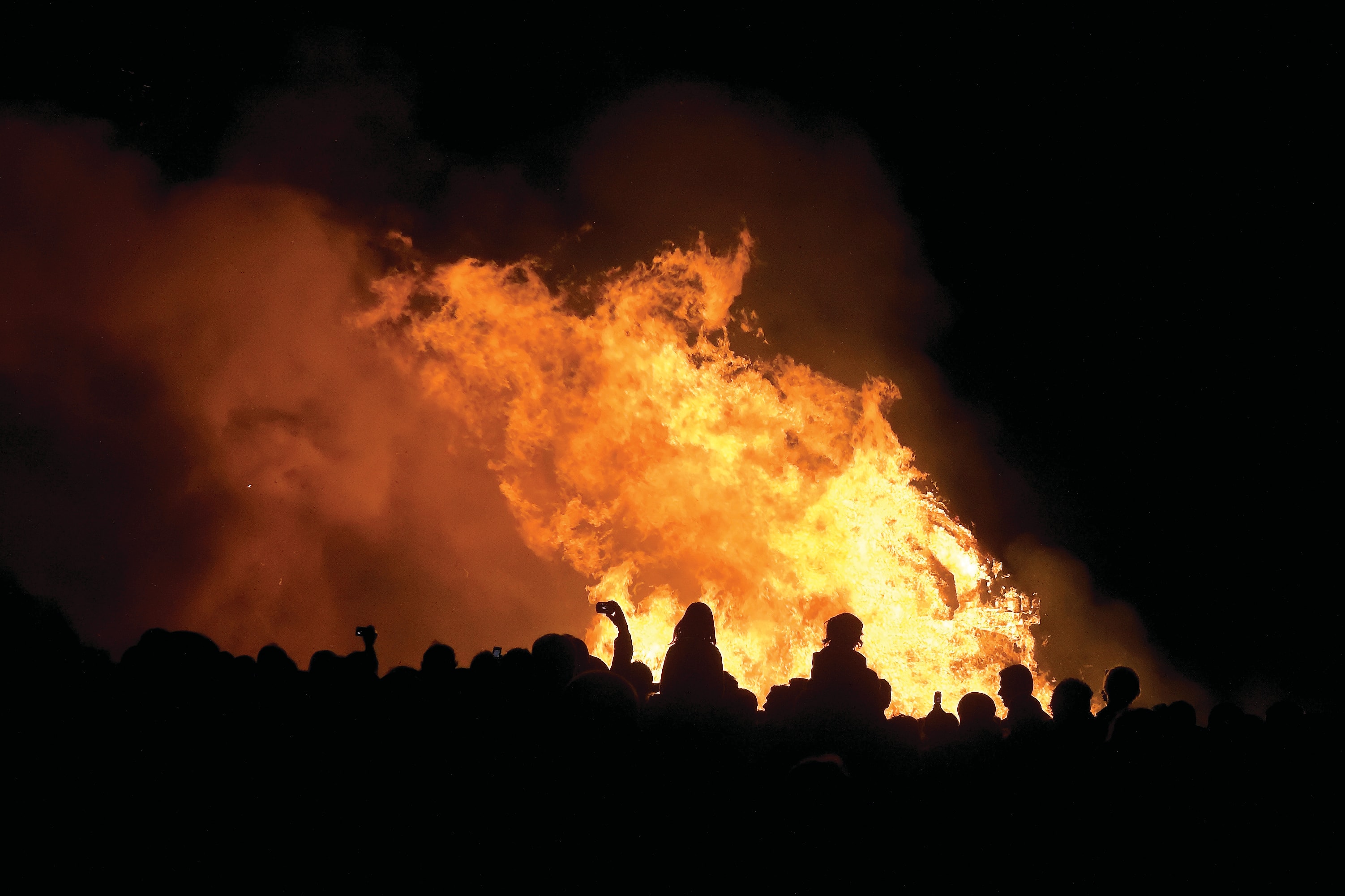 Large bonfire lighting up the night as a crowd gathers around watching.