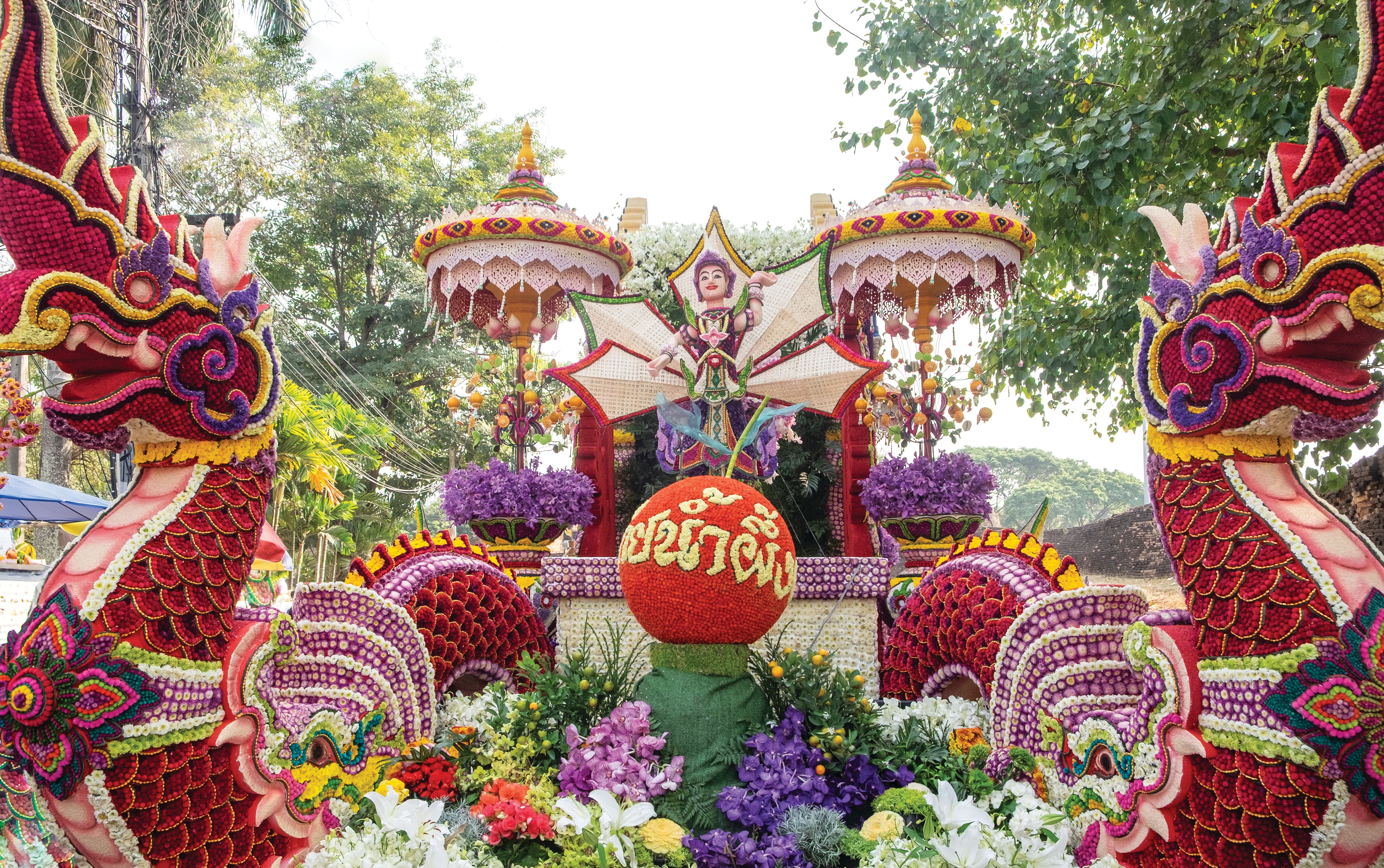 Bright and colourful flower display with dragon-like sculptures, decorative umbrellas and floral arrangements at an outdoor festival.