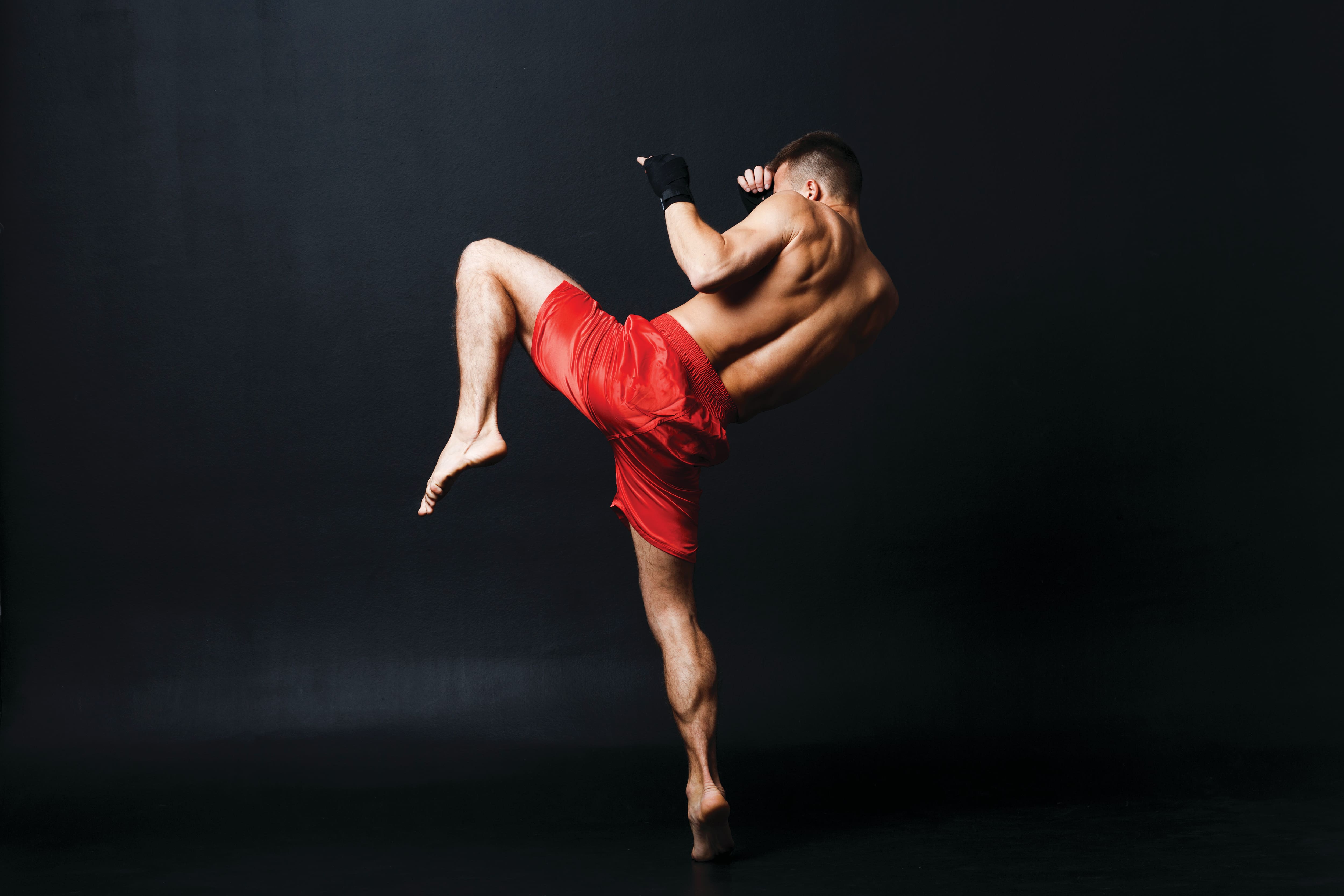 Person performing a high kick in red shorts against a dark background.