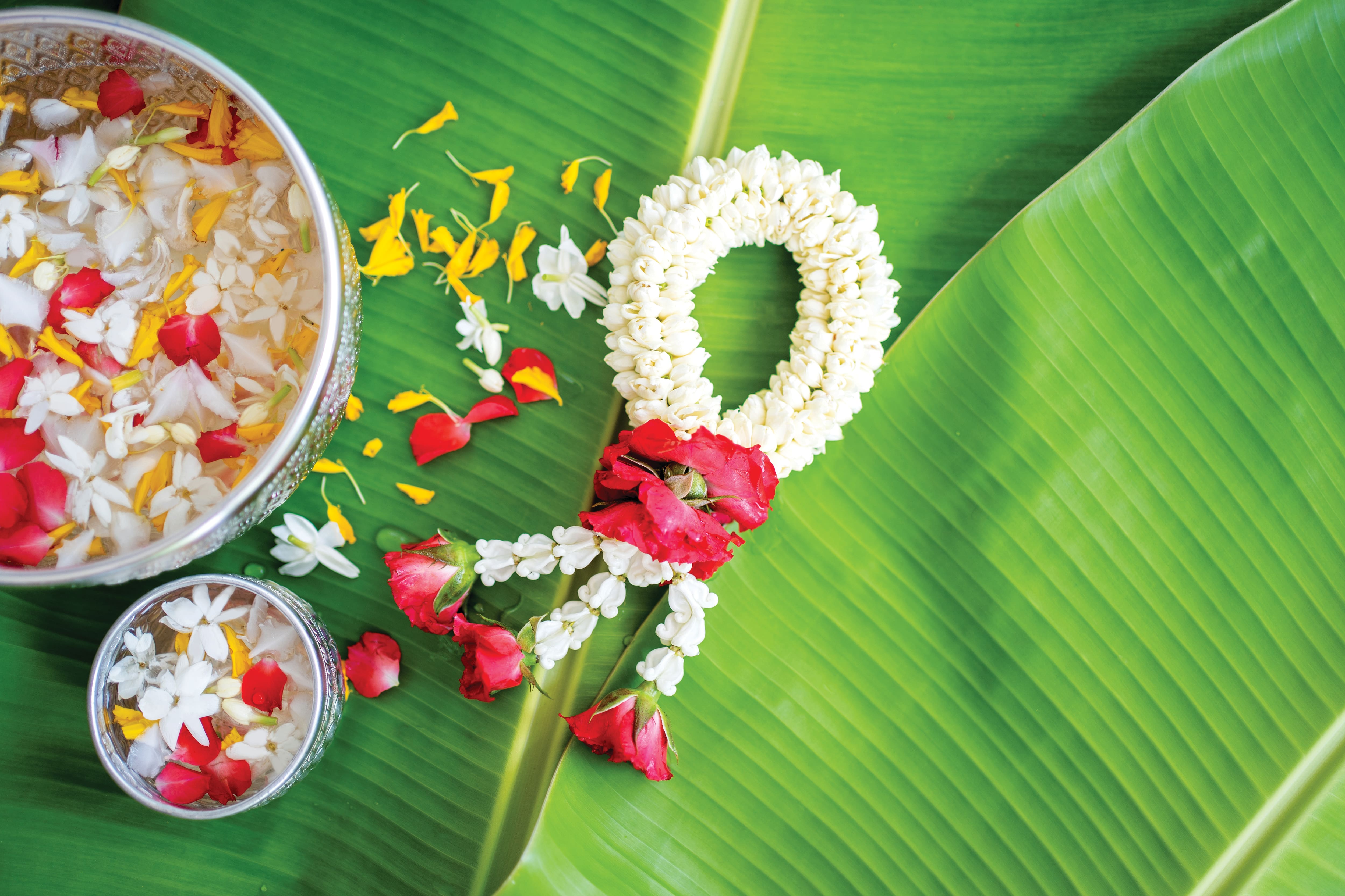 Flower garland and floating petals on large green leaves.