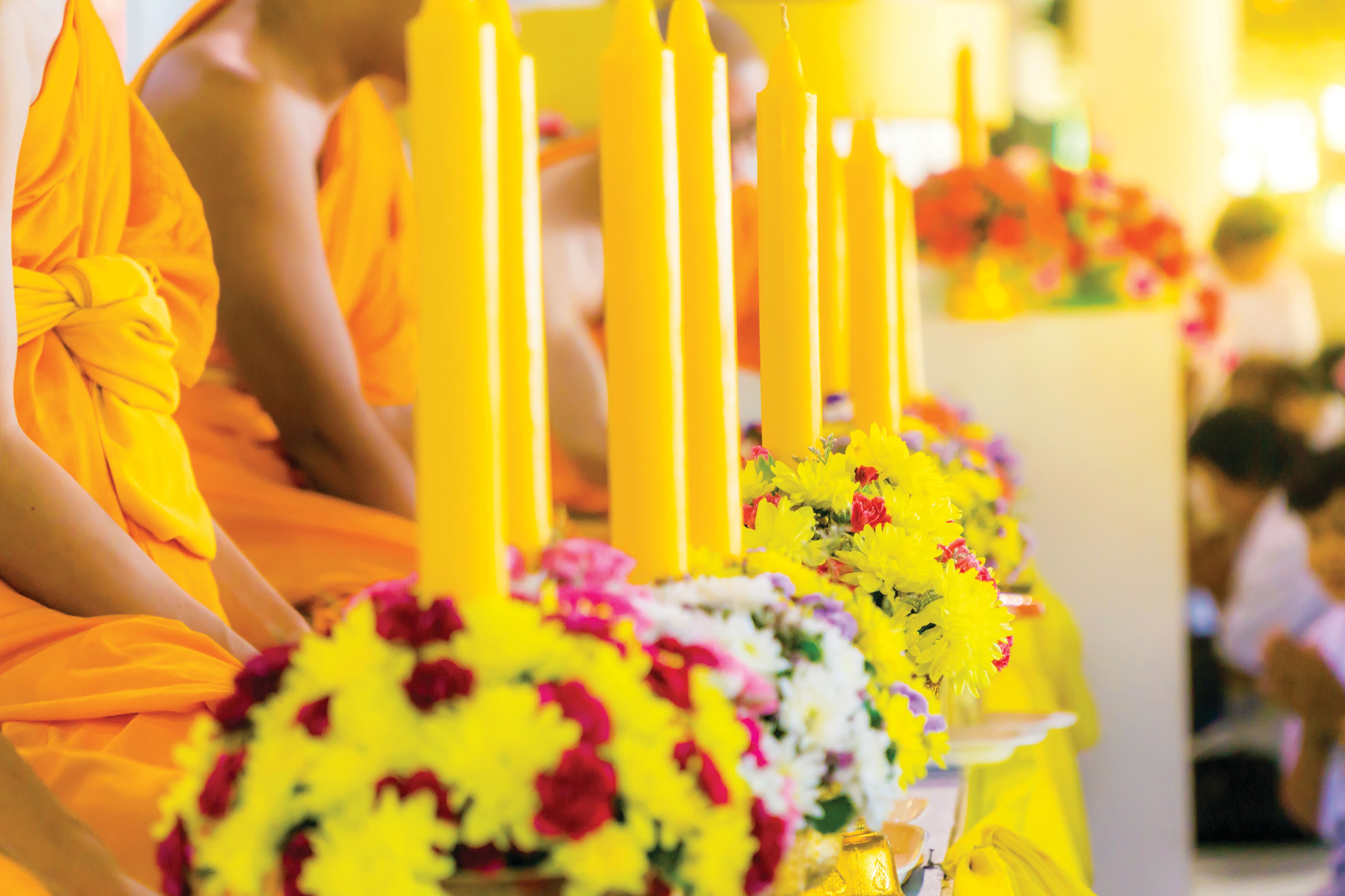 Candles and flowers arranged in front of Buddhist monks during a ceremony.