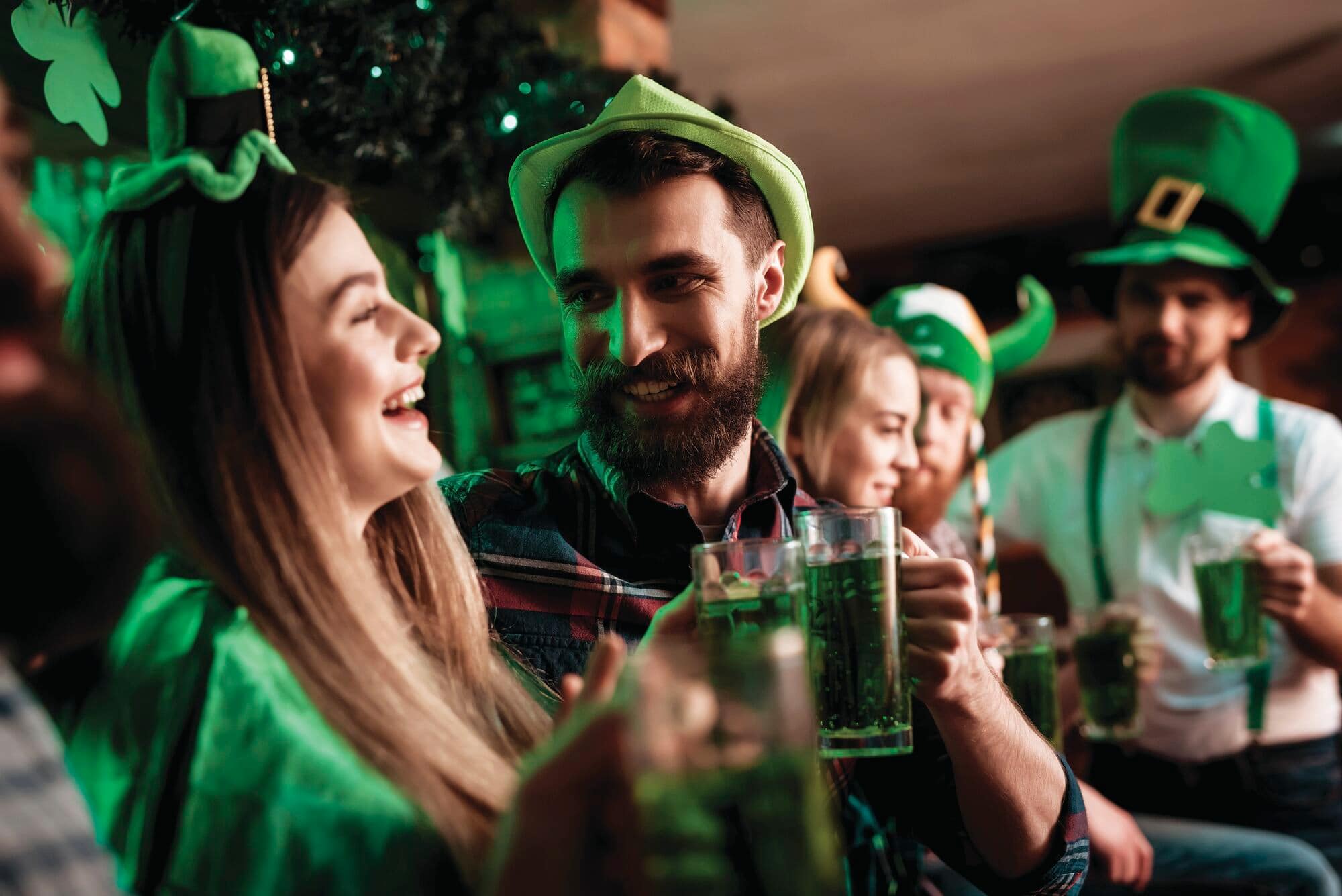 People celebrating St Patrick’s Day in a pub, wearing green hats and holding drinks.