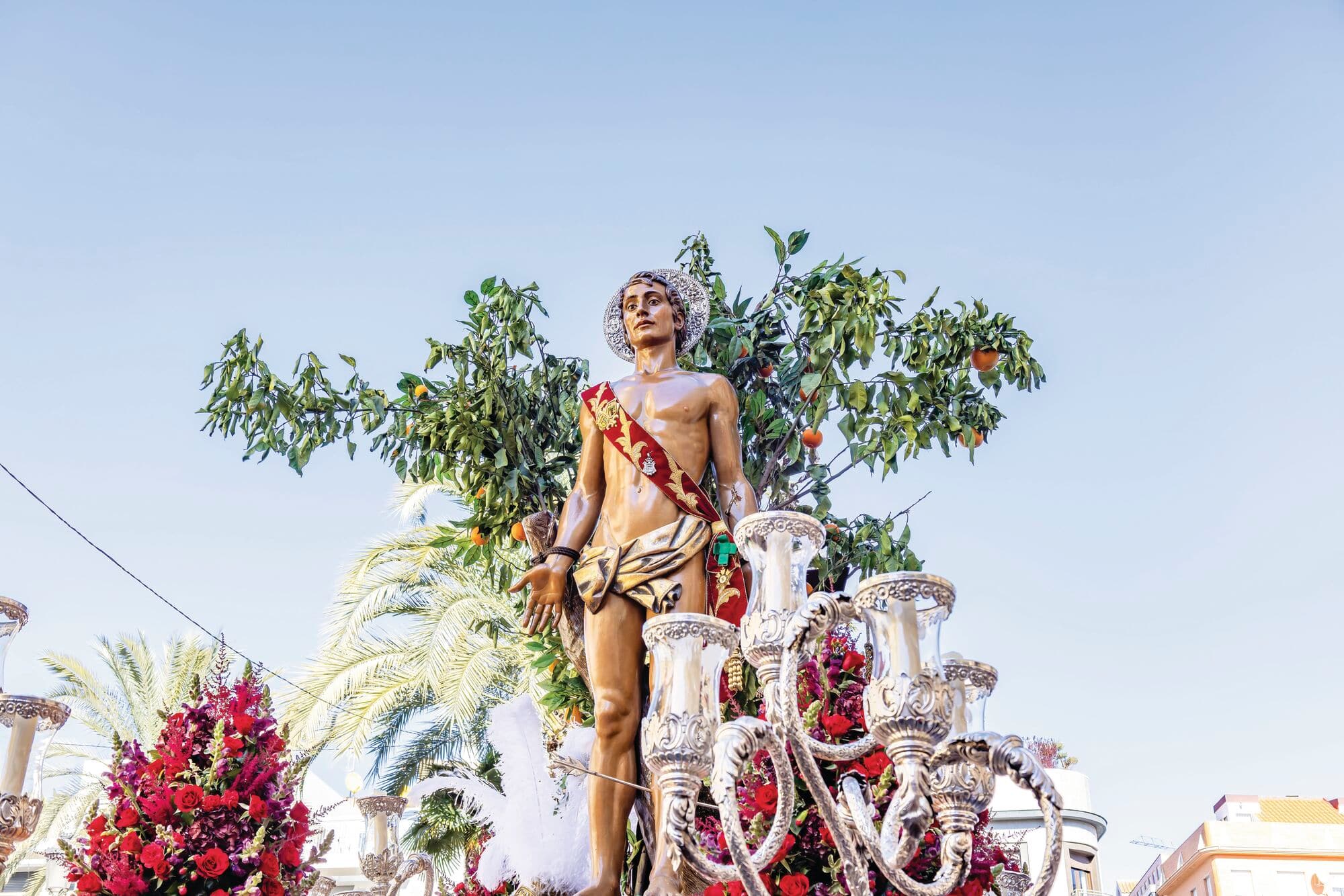 Statue of St Sebastian being carried in street parade on a sunny day.