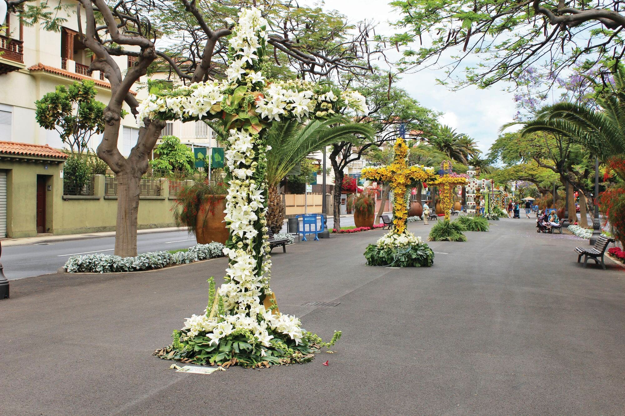 Image of street with large crosses placed along the centre covered with colourful displays of flowers.