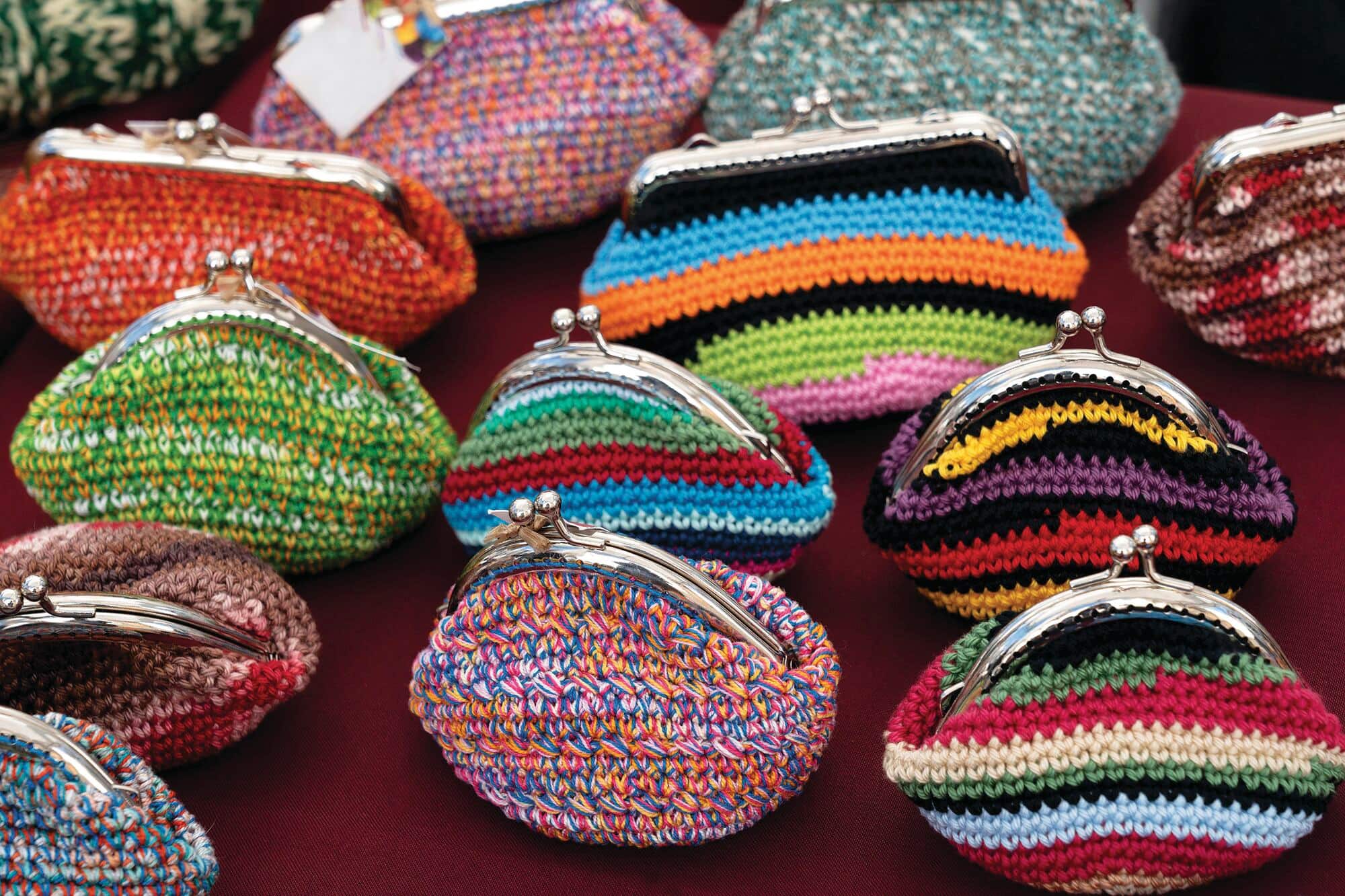 Colourful handmade coin purses with metal clasp closures displayed on a market stall. Each purse features vibrant knitted patterns in a variety of colours, creating an eye-catching display of local crafts.