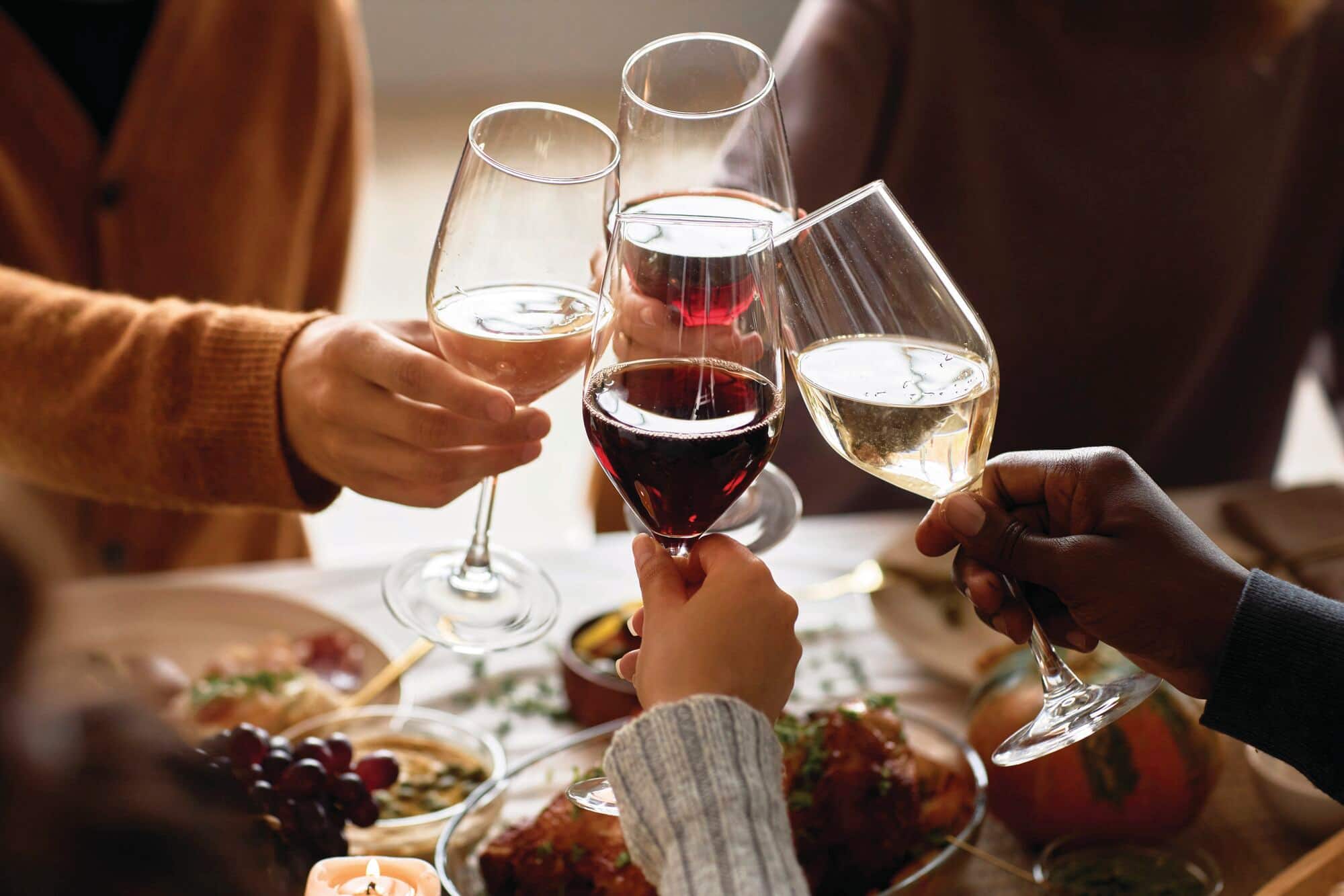 Four people toasting and holding wine glasses filled with different types of wine