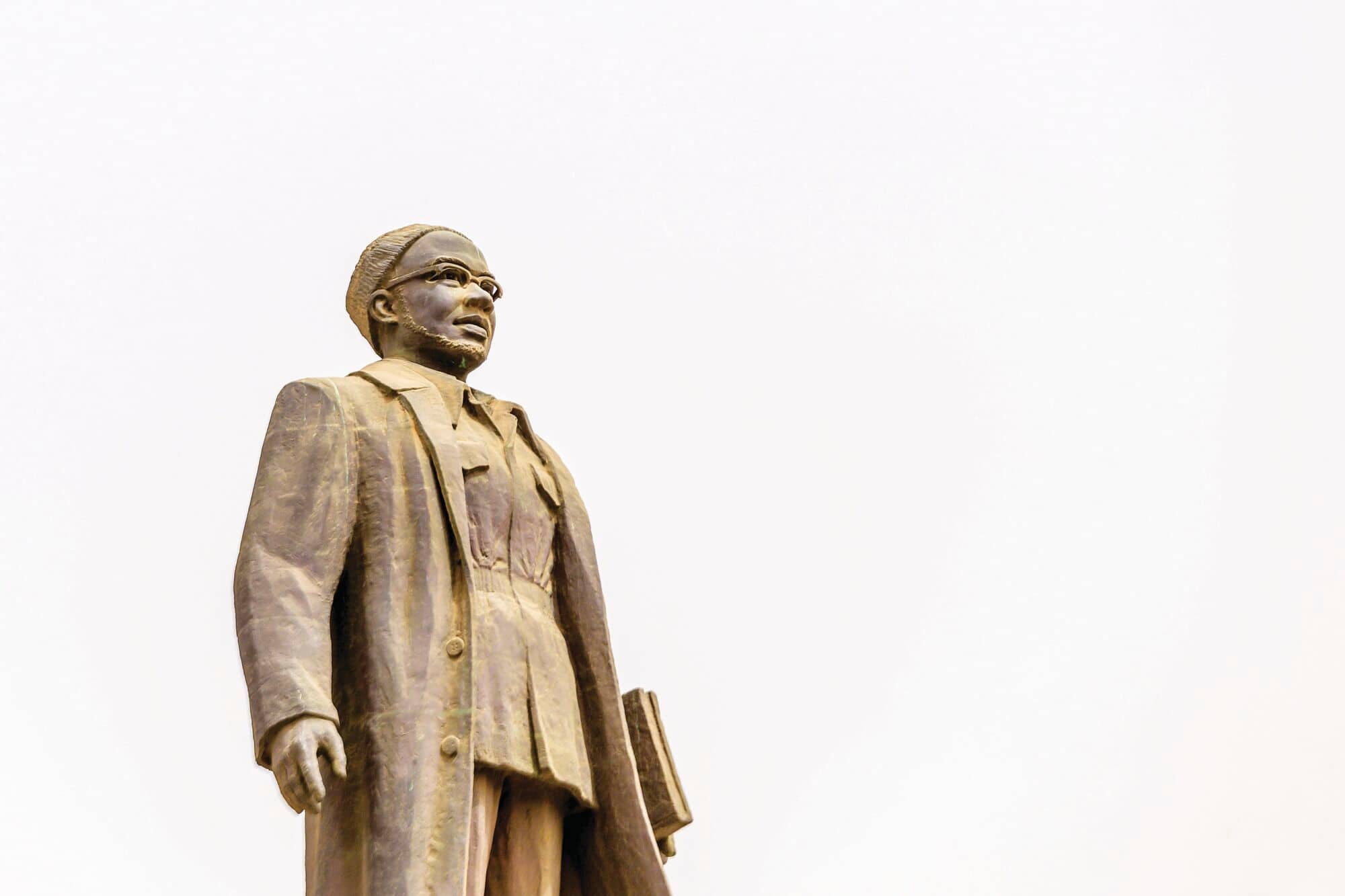 Bronze statue of a person in a long coat holding a book.
