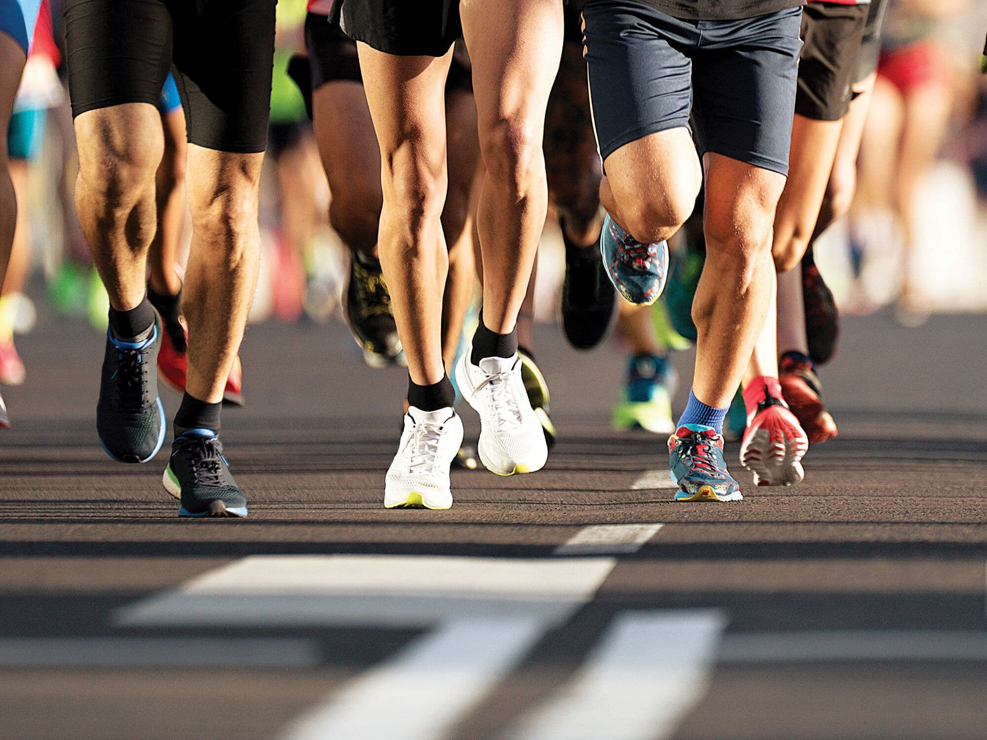 Close-up of runners' legs and trainers during a road race, with multiple participants running together on a paved course.