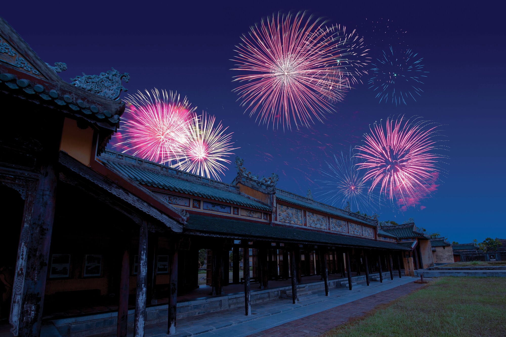 Fireworks light up the night sky above a historic building with traditional architecture, creating a colourful display over the illuminated courtyard.
