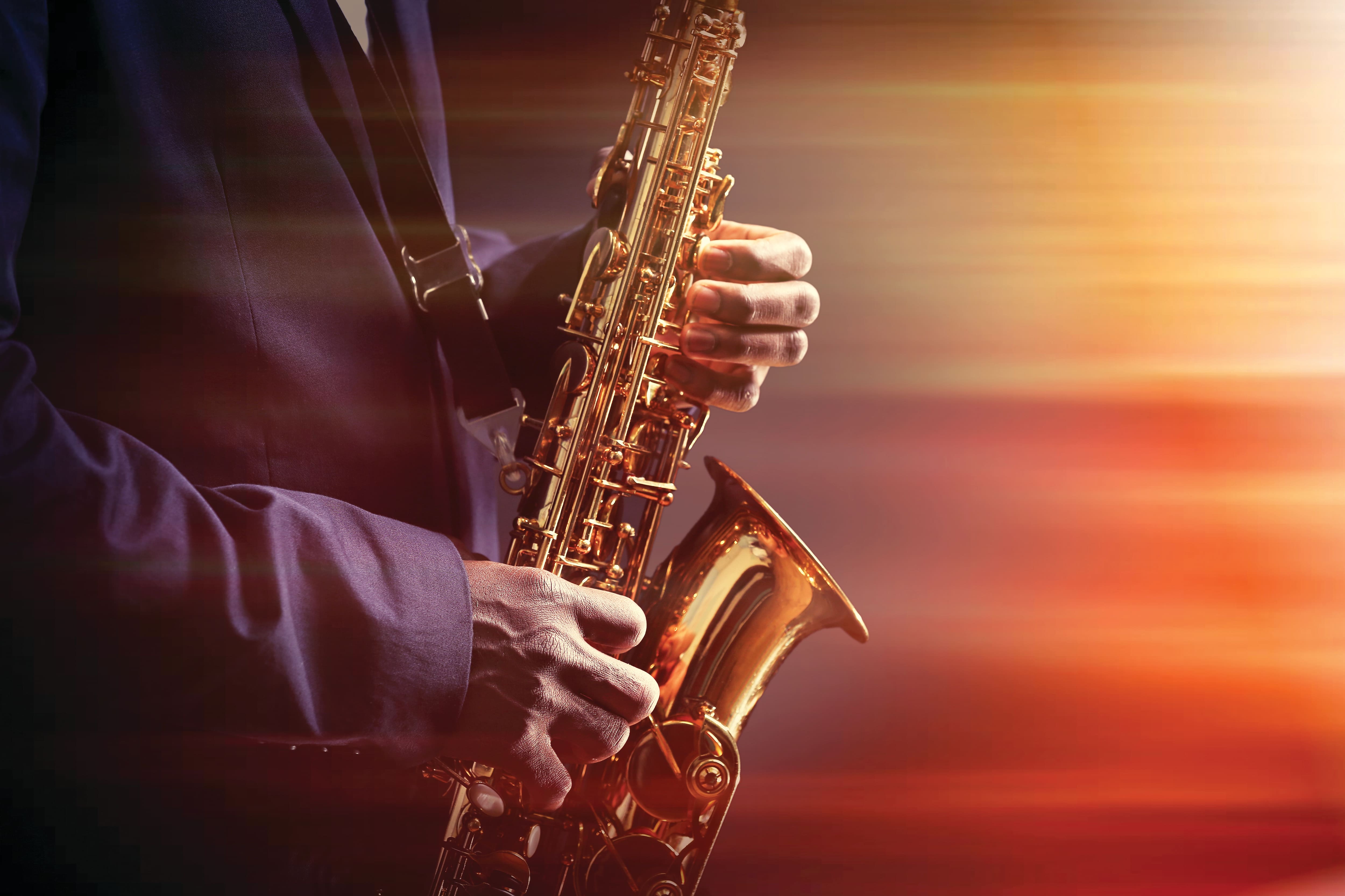 Person playing a saxophone under warm stage lighting.