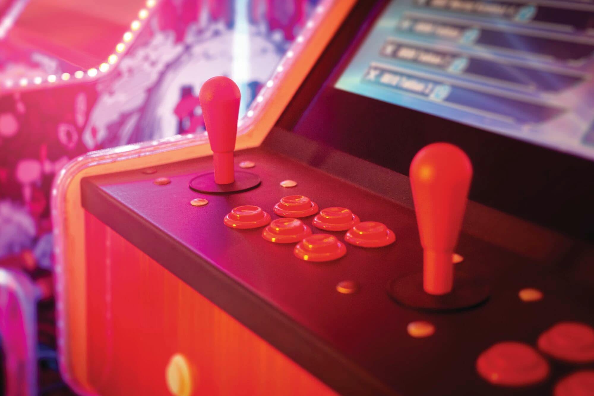 A close-up of a retro-style arcade machine control panel with red joysticks and round pushbuttons
