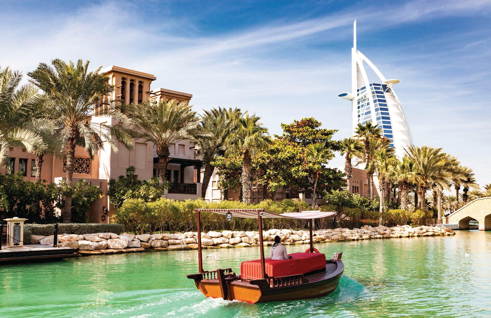 A wooden abra boat riding on the water canals at Madinat Jumeirah with the Burj Al Arab hotel in the background