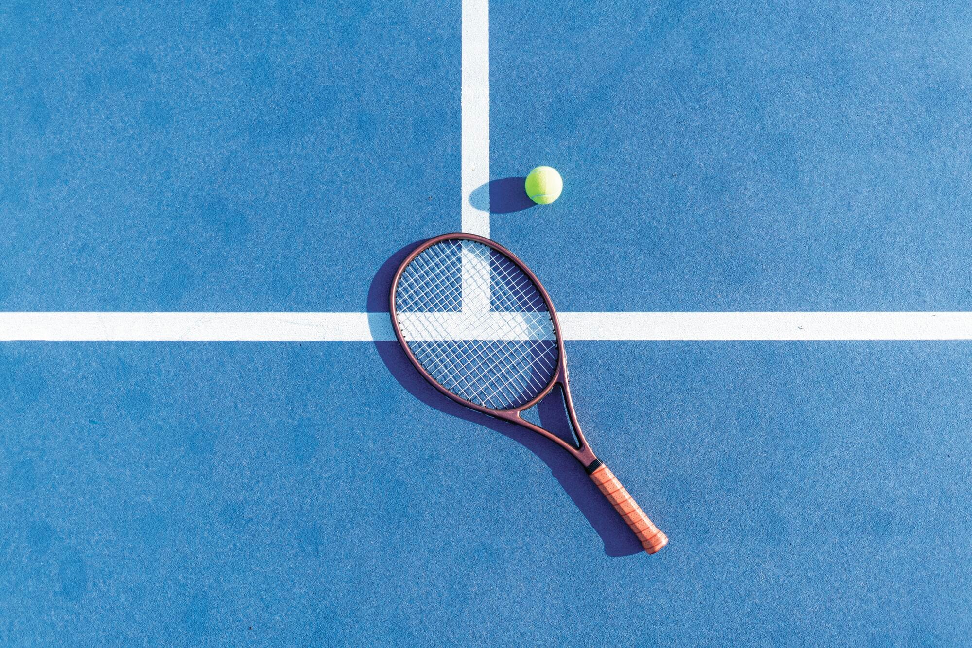 A tennis racket lays flat on a blue hardcourt