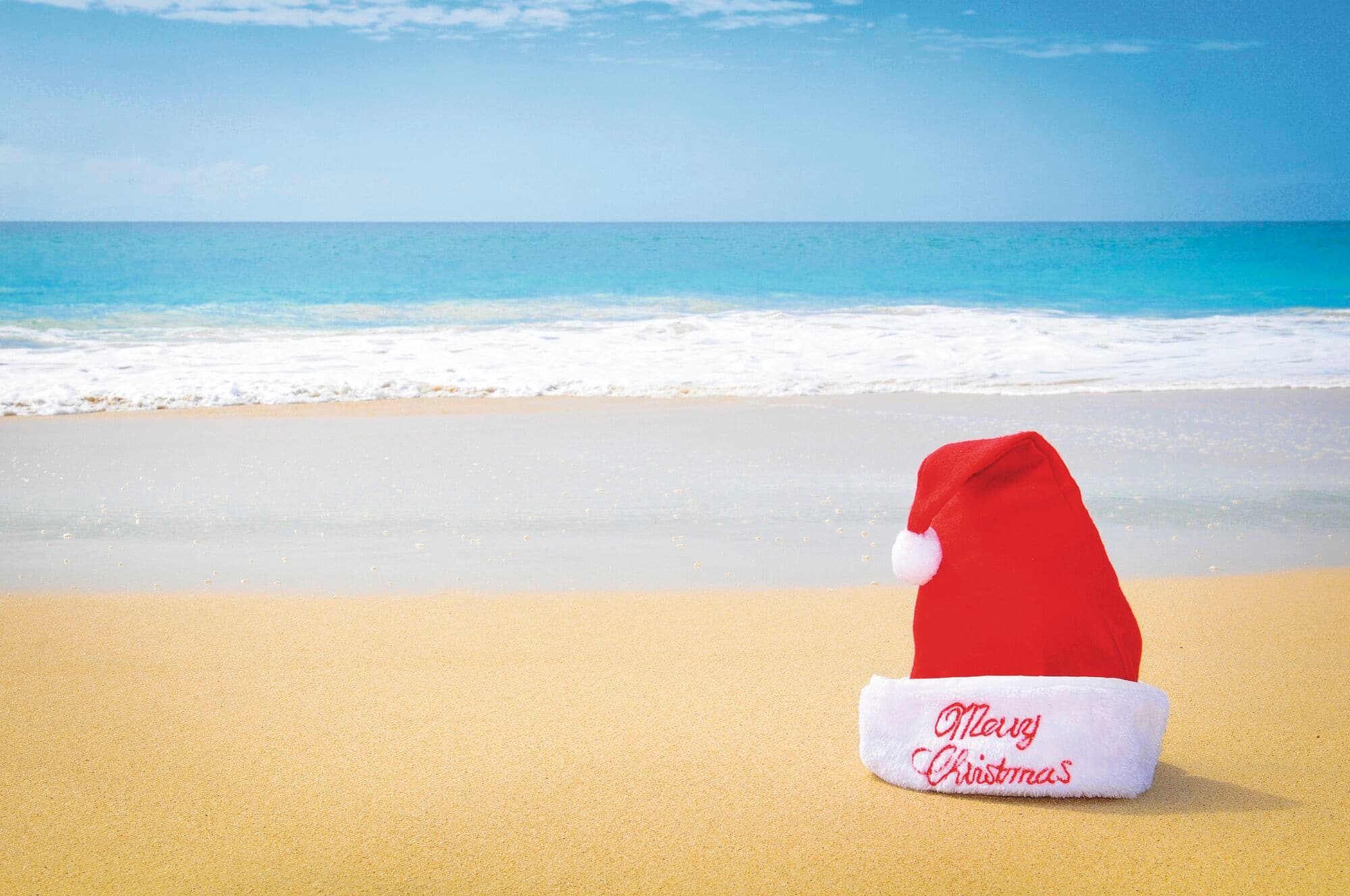 Santa hat on a sandy beach by the sea.