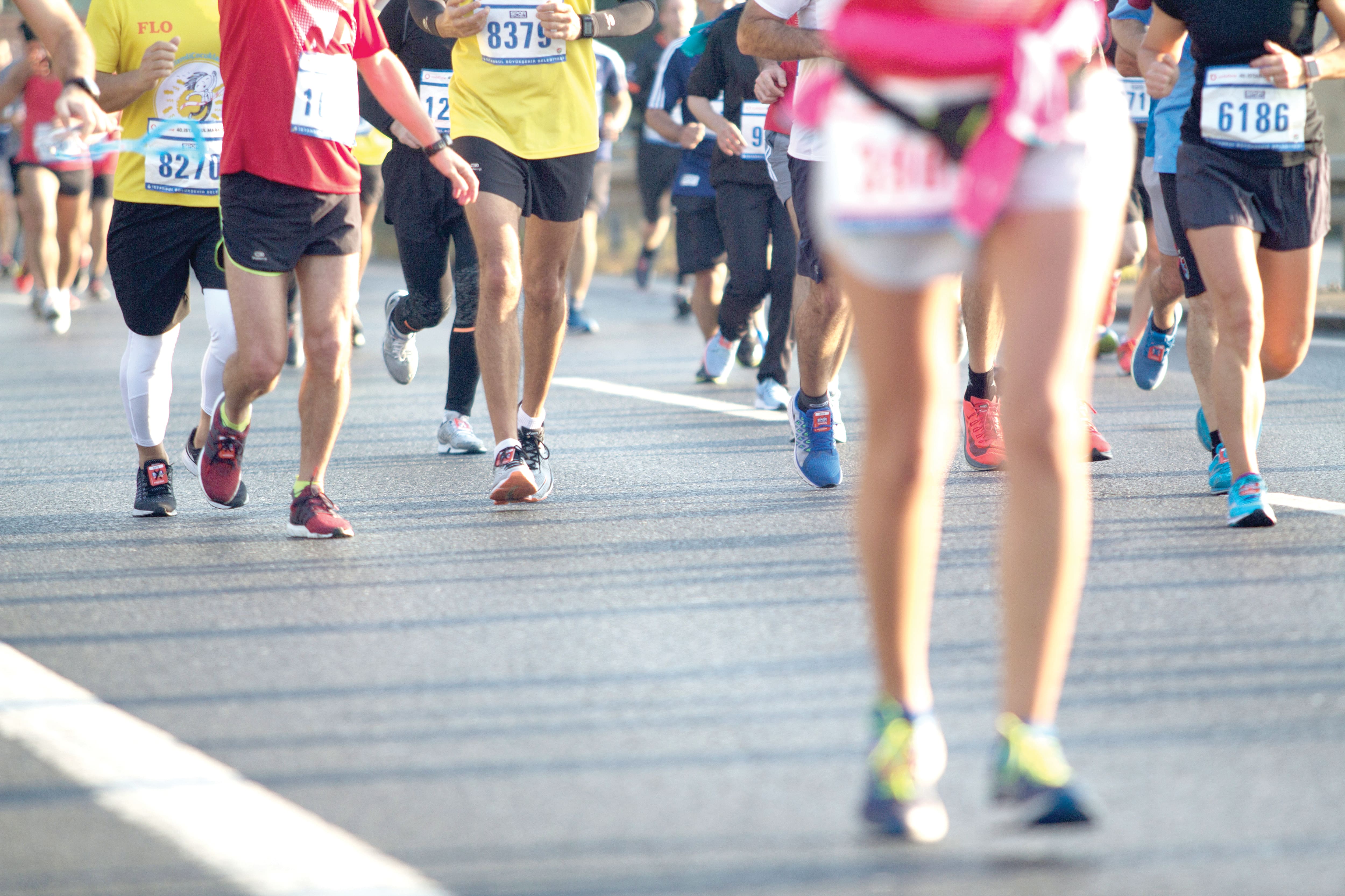 Participants run along a closed road during a large organised road race, wearing numbered bibs and brightly coloured sportswear. 