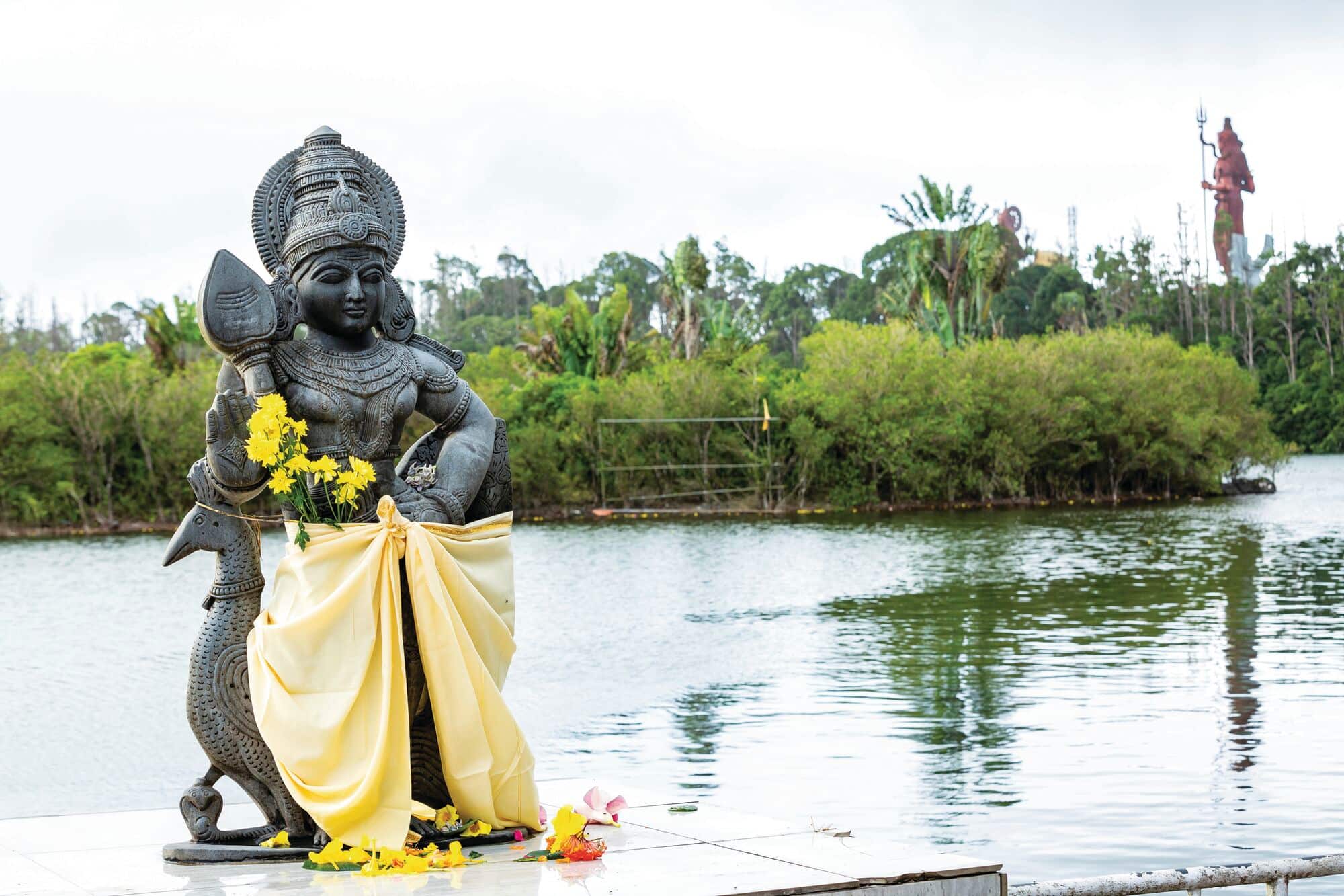 Religious Hindu statue beside a lake, decorated with yellow flowers and draped fabric.