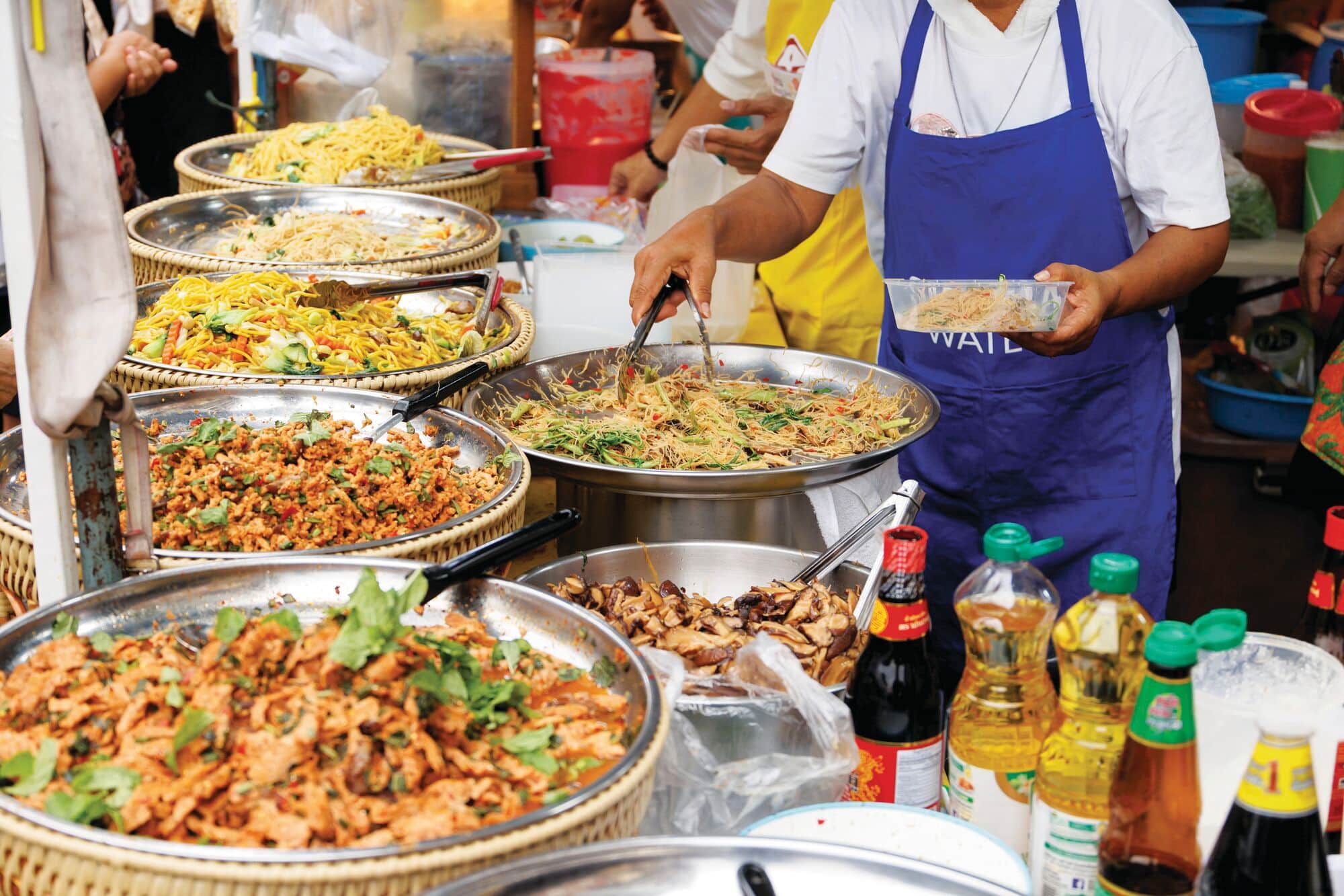 Street food stall serving a variety of noodle dishes and cooked foods.