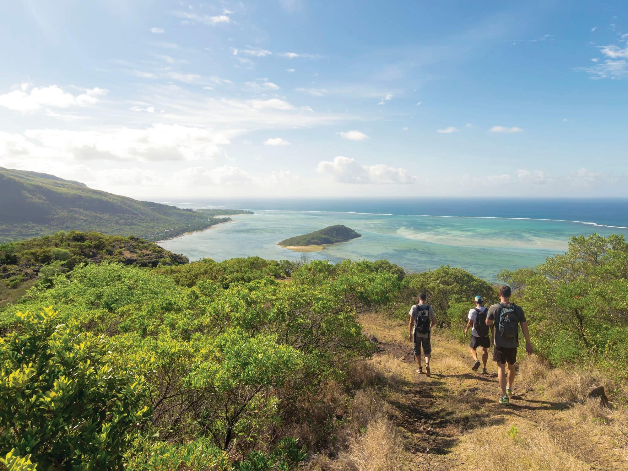 Hikers walking along a coastal trail overlooking turquoise waters and a small island.